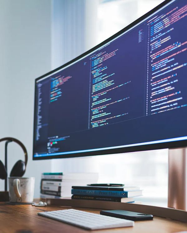 A workdesk with books, a keyboard and an extrawide monitor